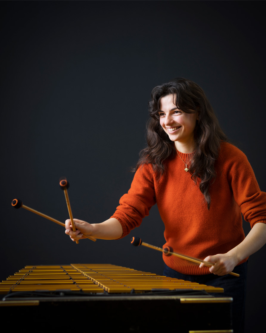 A women playing the marimba and smiling, looking to the side.